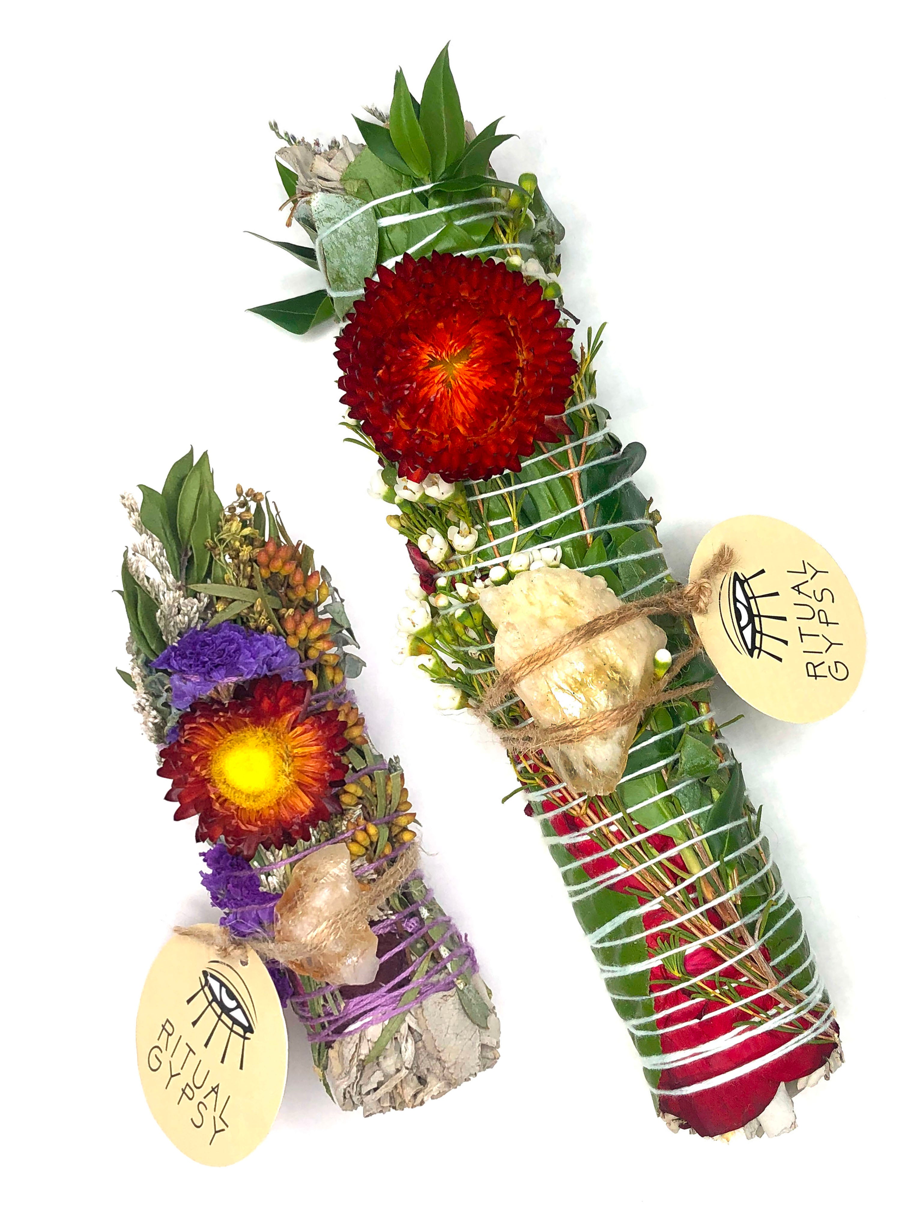 white sage smoke cleansing smudge bundle wrapped in florals with orange red strawflower and orange yellow citrine crystal and round ritual gypsy product tag attached on white background