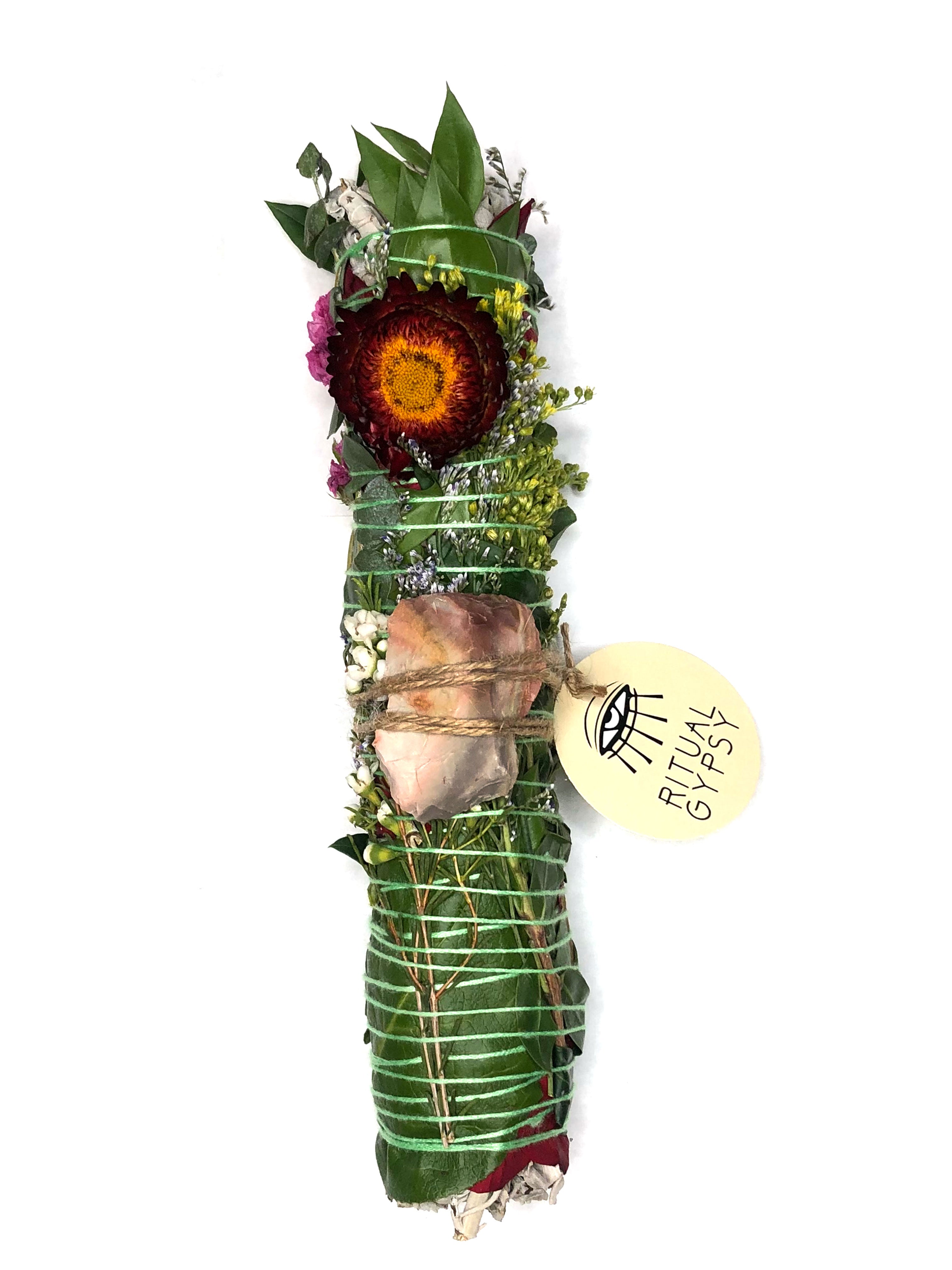 white sage smoke cleansing smudge bundle wrapped in florals with orange red strawflower and orange brown gray desert jasper crystal and round ritual gypsy product tag attached on white background