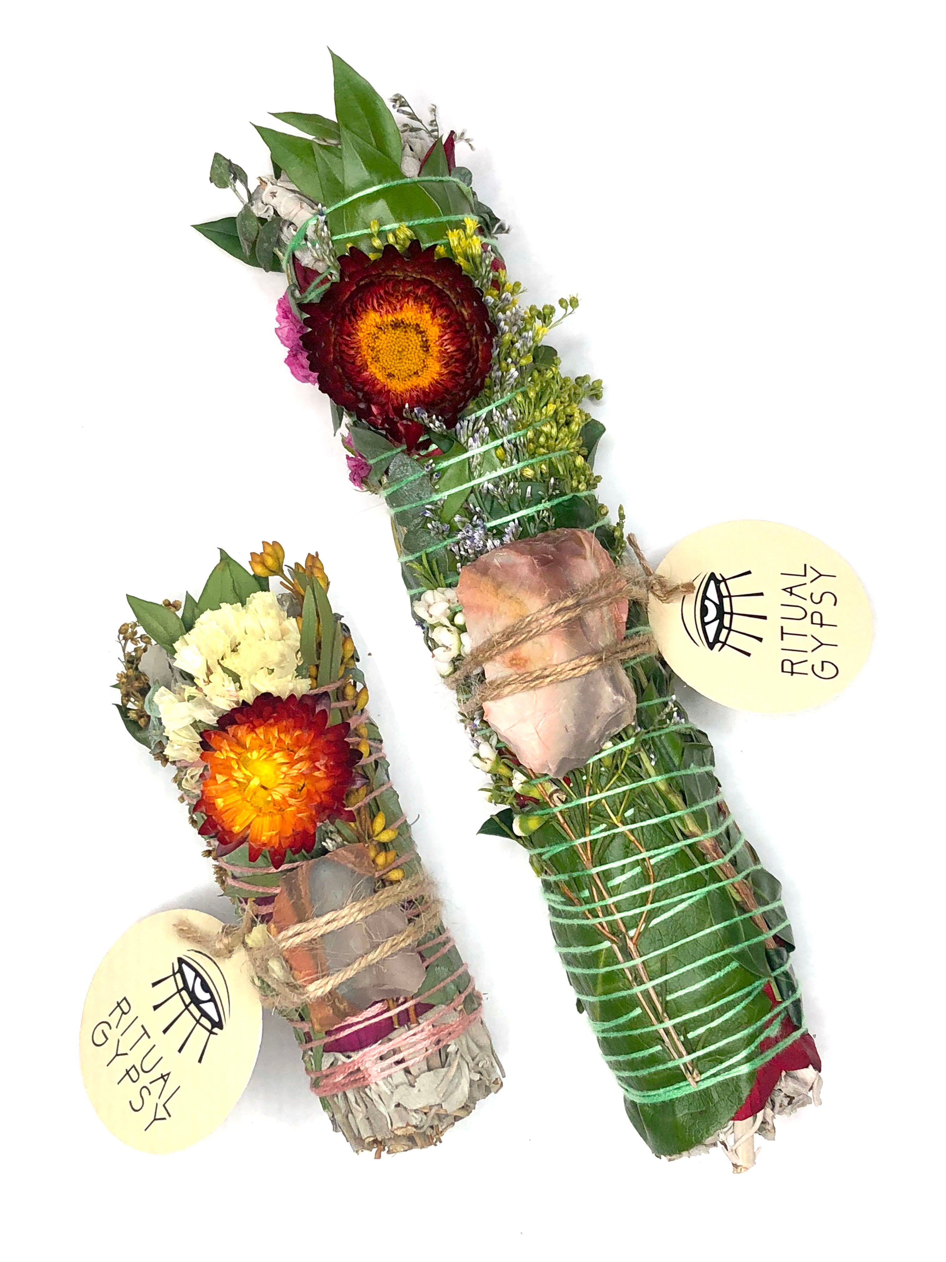 white sage smoke cleansing smudge bundle wrapped in florals with orange red strawflower and orange brown gray desert jasper crystal and round ritual gypsy product tag attached on white background
