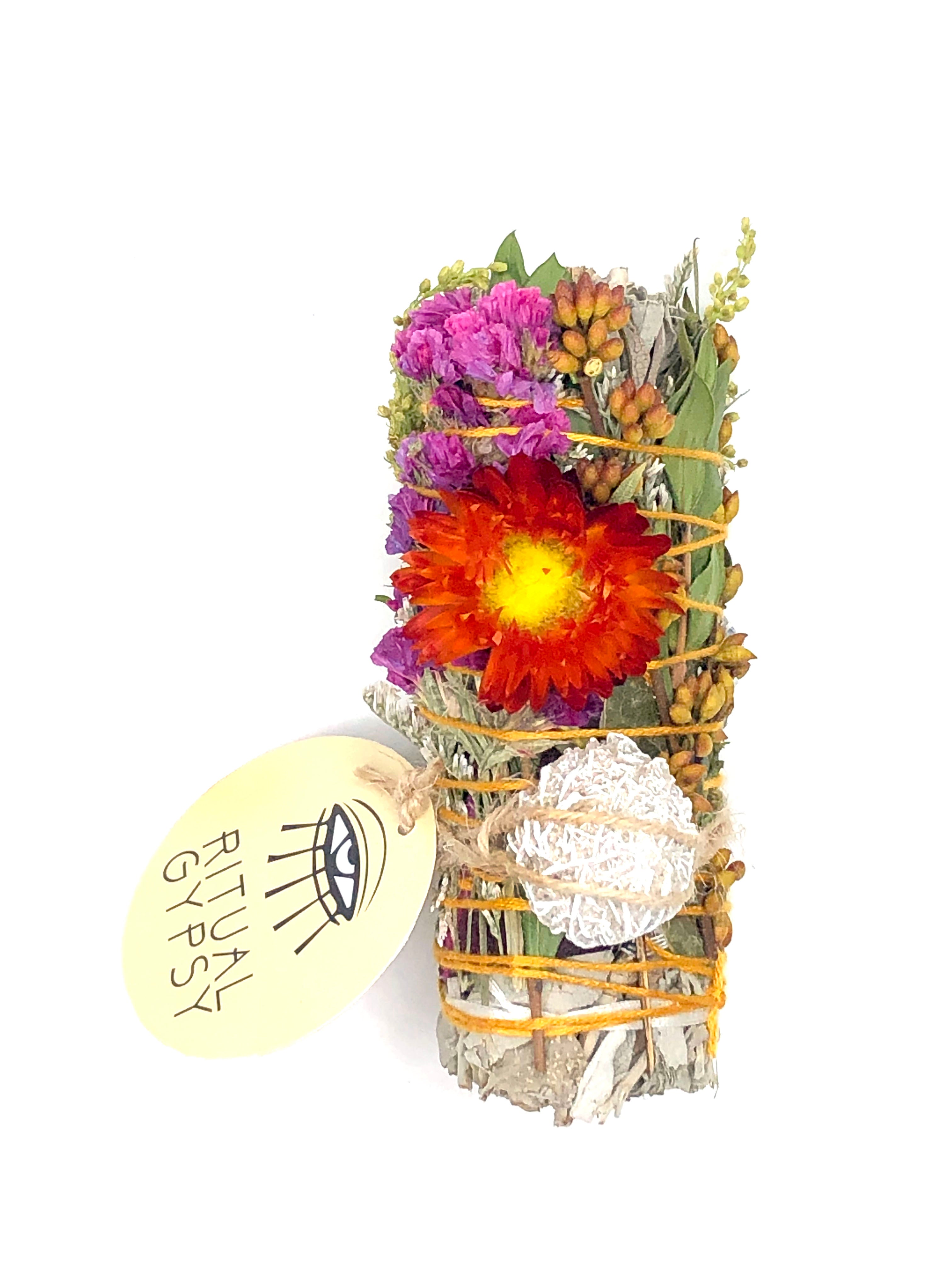 white sage smoke cleansing smudge bundle wrapped in rose petals and florals with gold pyrite crystal and round ritual gypsy product tag on white background