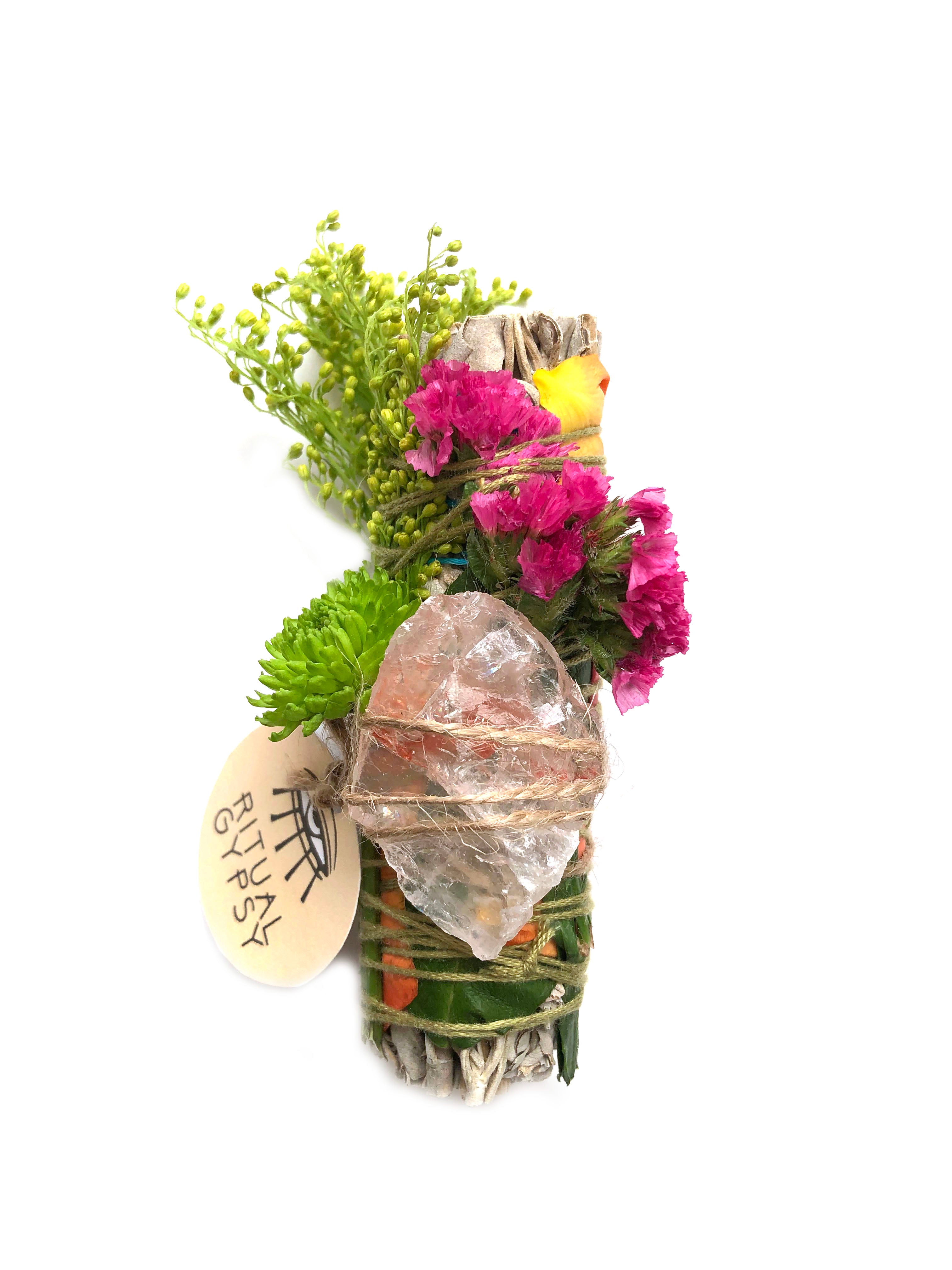 white sage smoke cleansing smudge bundle wrapped in florals with orange red strawflower and pink fire quartz crystal and round ritual gypsy product tag attached on white background