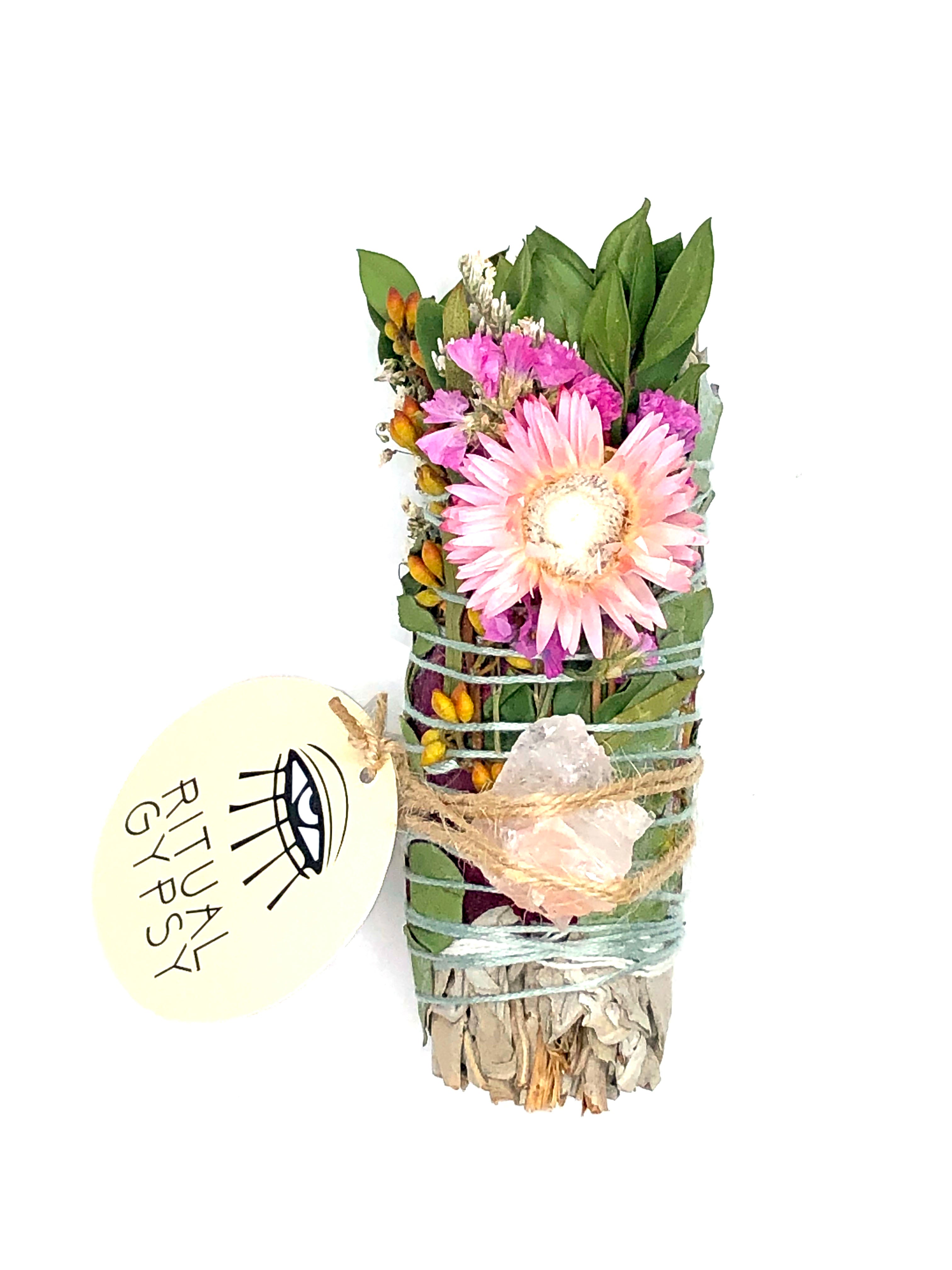 white sage smoke cleansing smudge bundle wrapped in florals with orange red strawflower and pink fire quartz crystal and round ritual gypsy product tag attached on white background