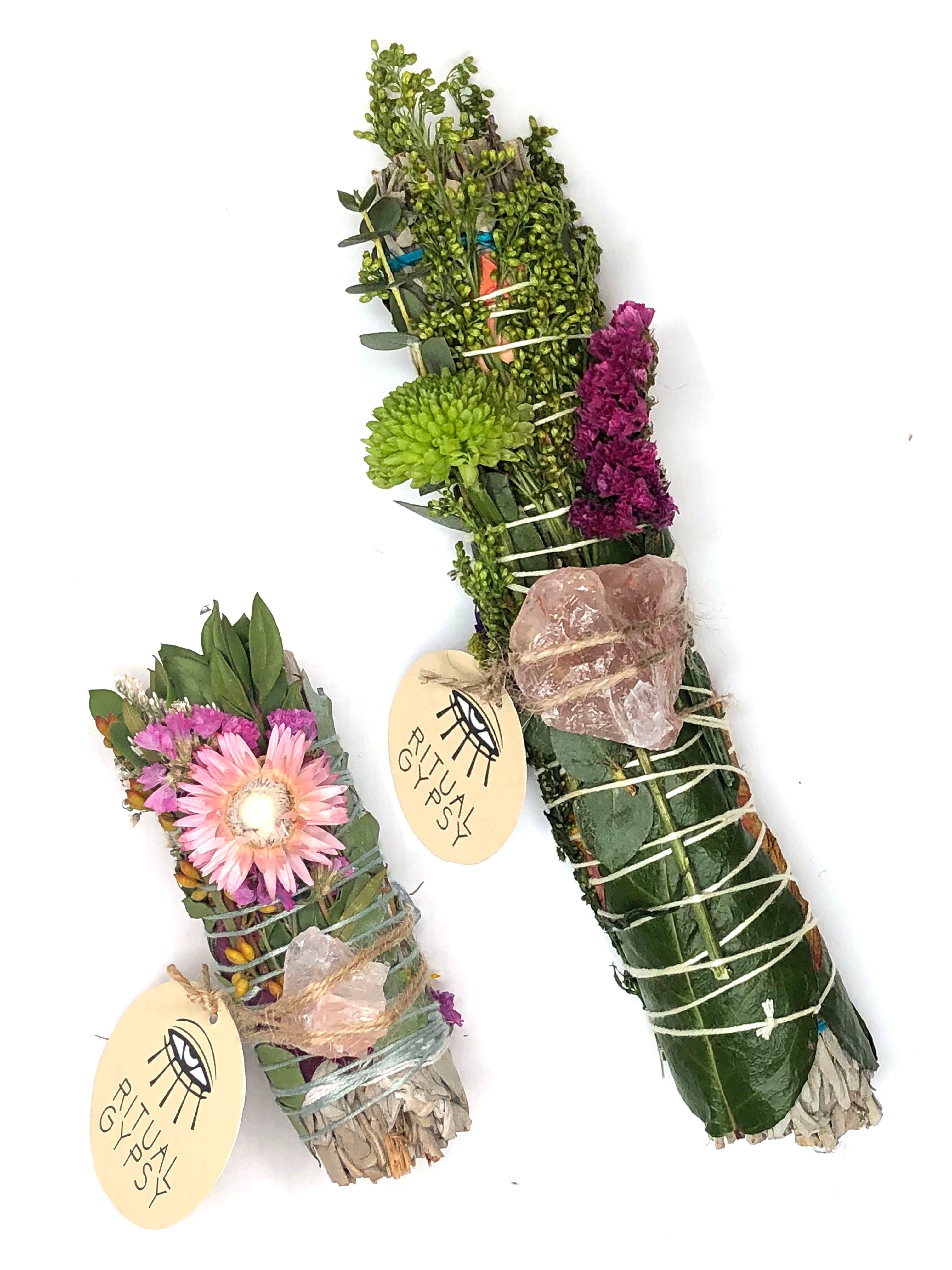 white sage smoke cleansing smudge bundle wrapped in florals with orange red strawflower and pink fire quartz crystal and round ritual gypsy product tag attached on white background