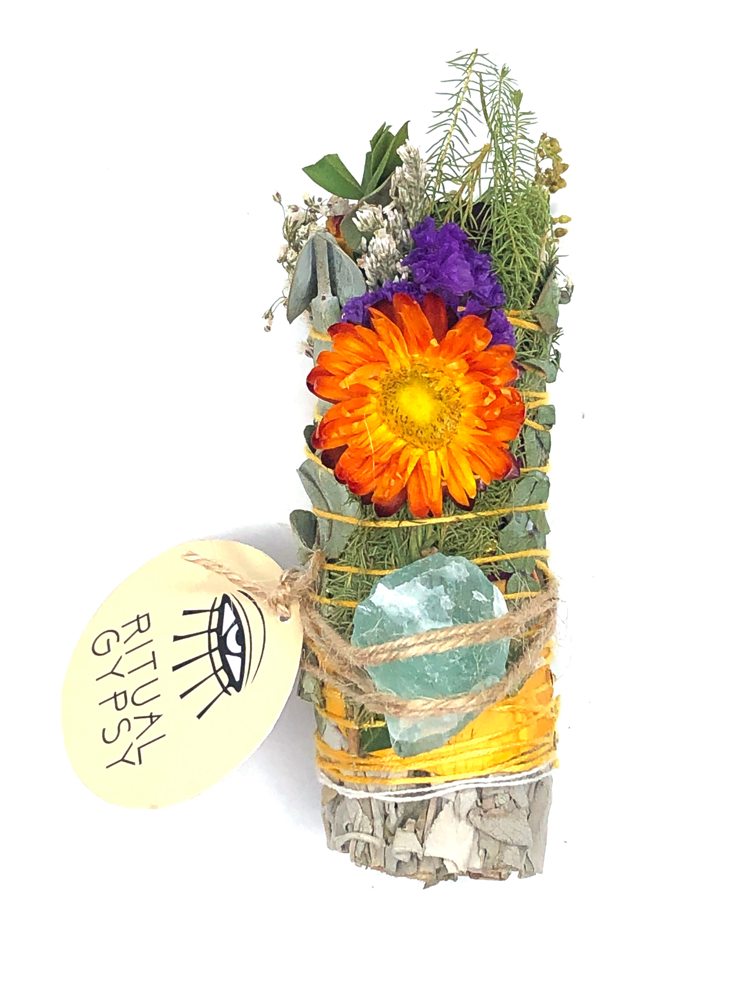white sage smoke cleansing smudge bundle wrapped in florals with orange red strawflower and blue purple green fluorite crystal and round ritual gypsy product tag attached on white background