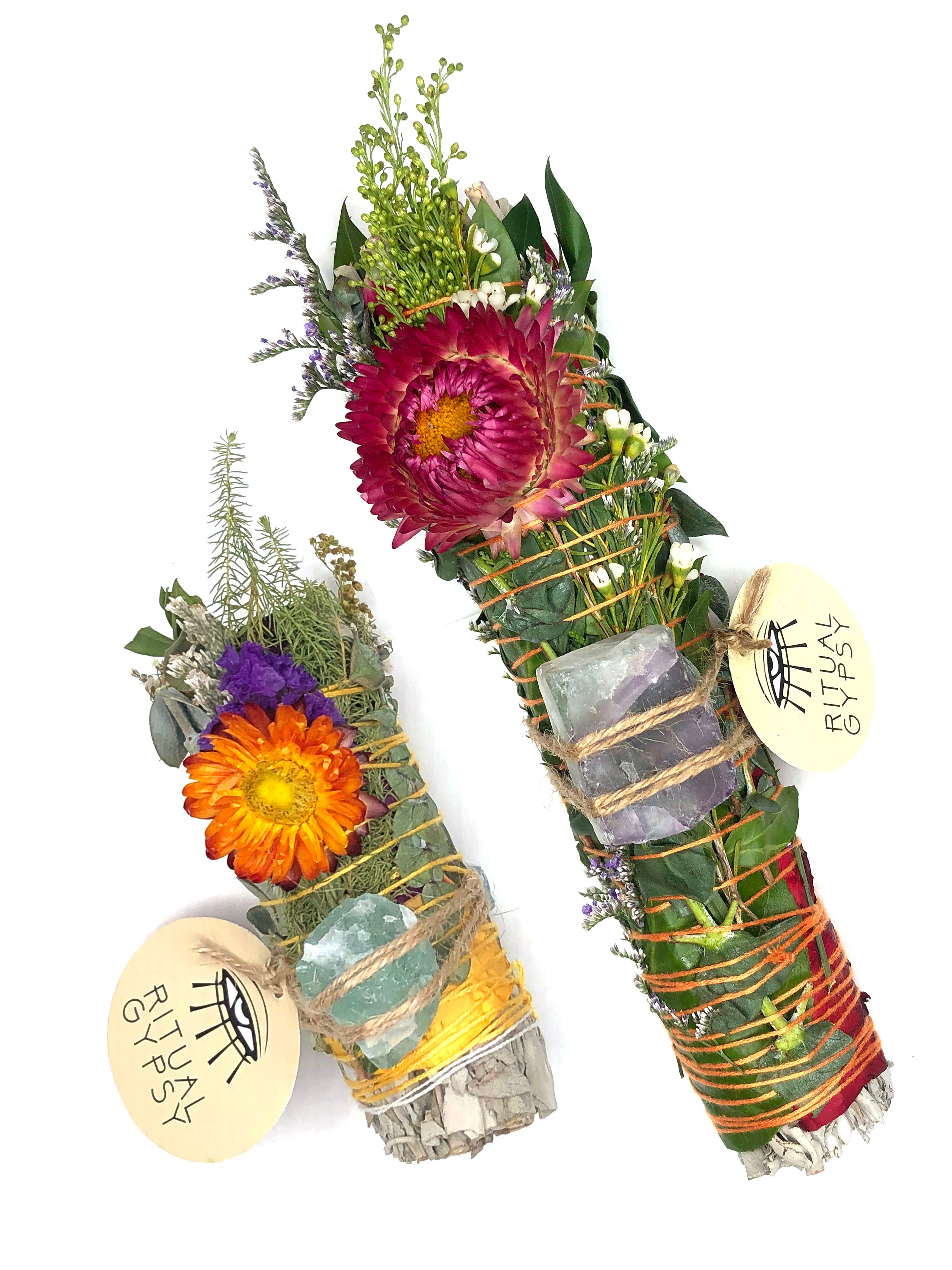 white sage smoke cleansing smudge bundle wrapped in florals with orange red strawflower and blue purple green fluorite crystal and round ritual gypsy product tag attached on white background