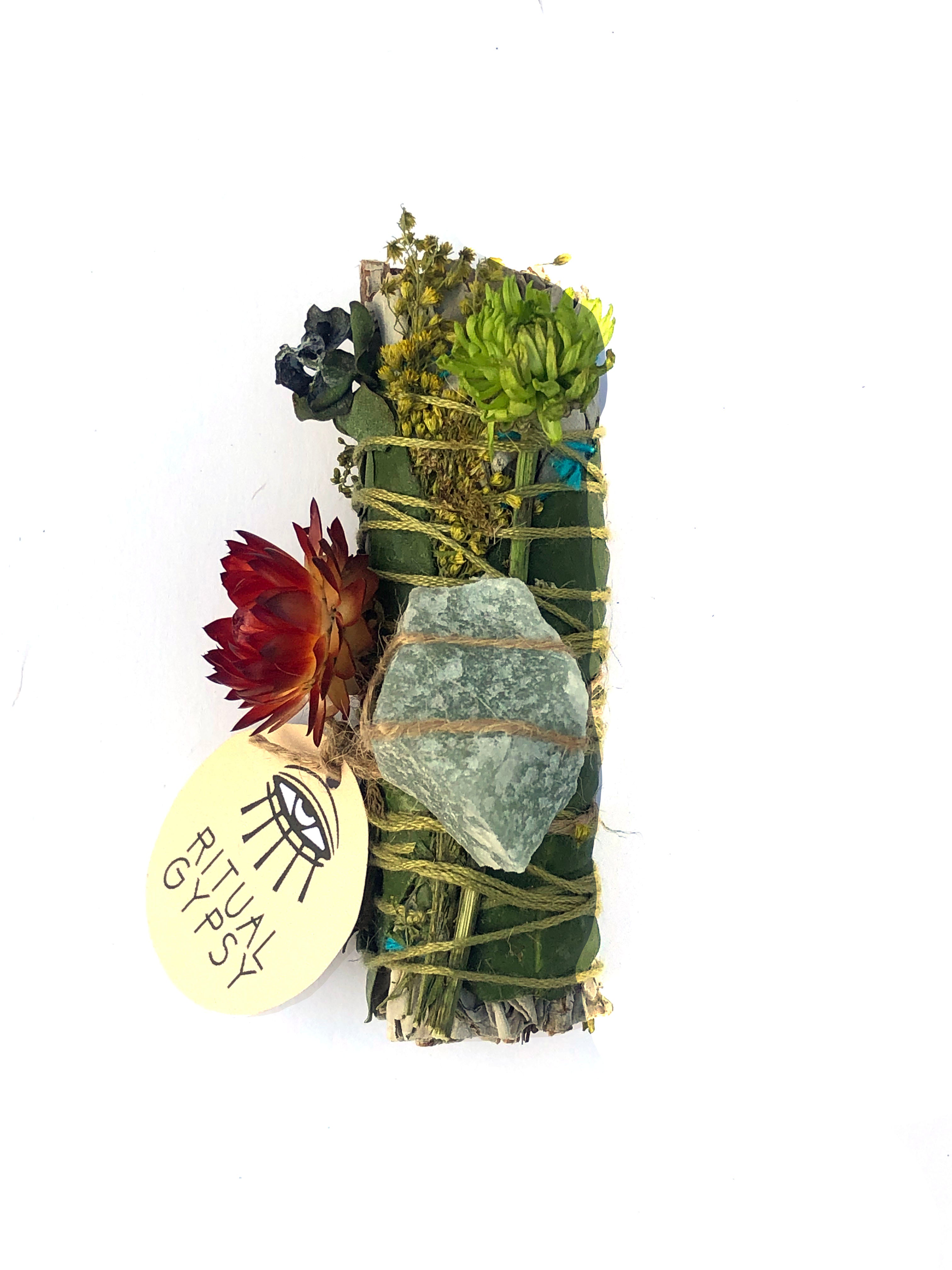 white sage smoke cleansing smudge bundle wrapped in florals with orange red strawflower and green aventurine crystal and round ritual gypsy product tag attached on white background