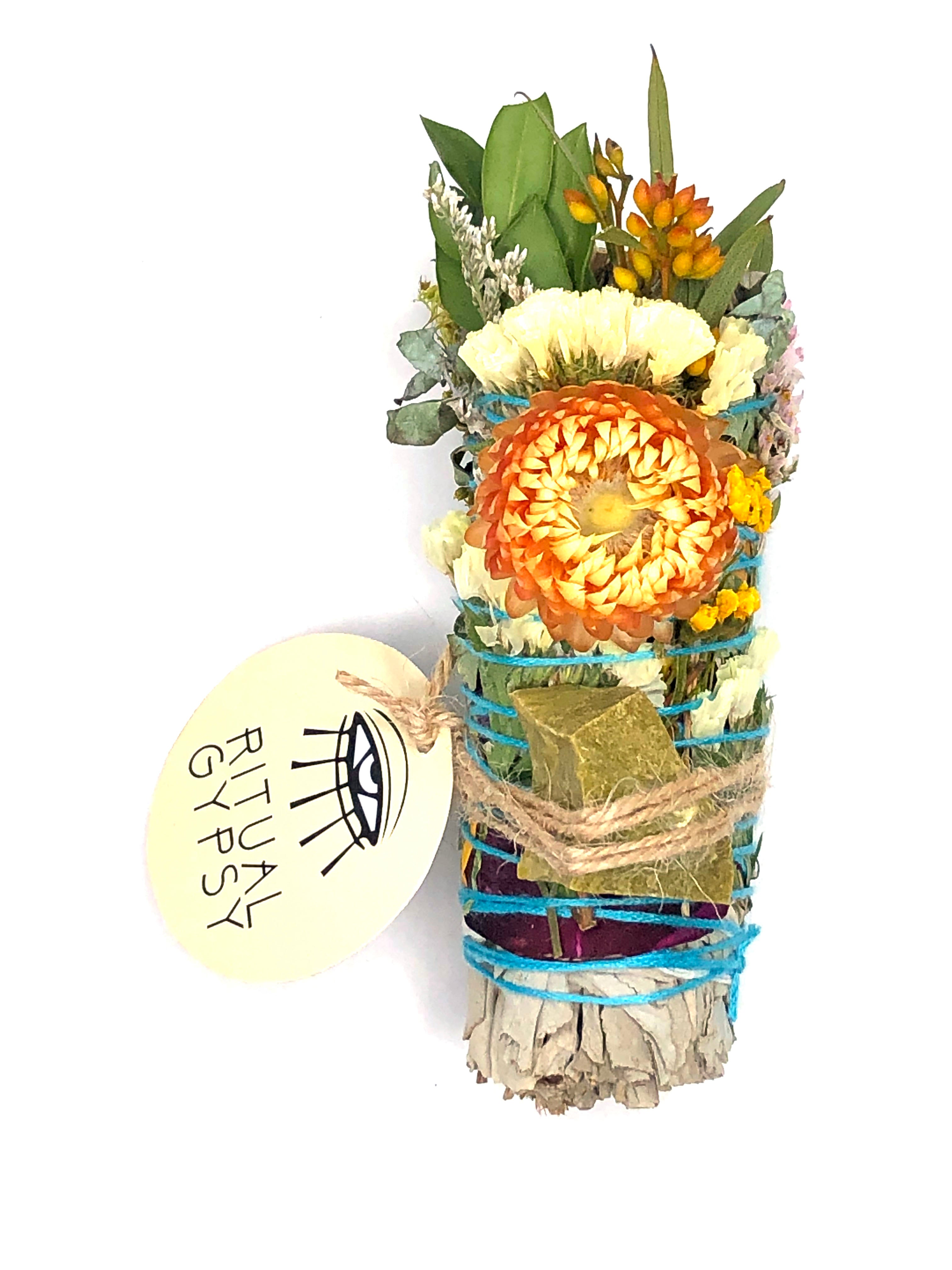 white sage smoke cleansing smudge bundle wrapped in florals with orange strawflower and green opal crystal and round ritual gypsy product tag attached on white background