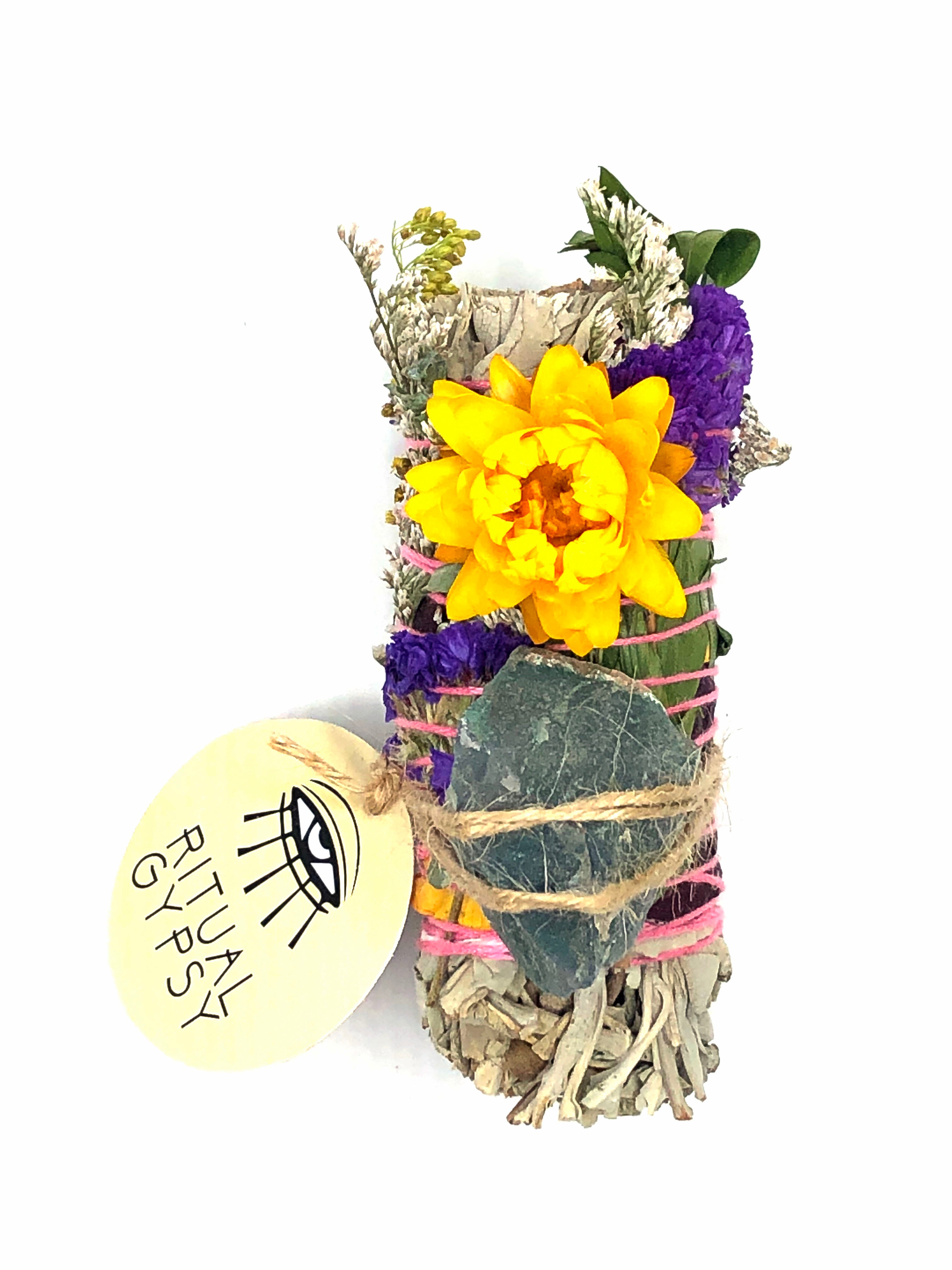 white sage smoke cleansing smudge bundle wrapped in florals with yellow strawflower and green moss crystal stone and round ritual gypsy product tag attached on white background