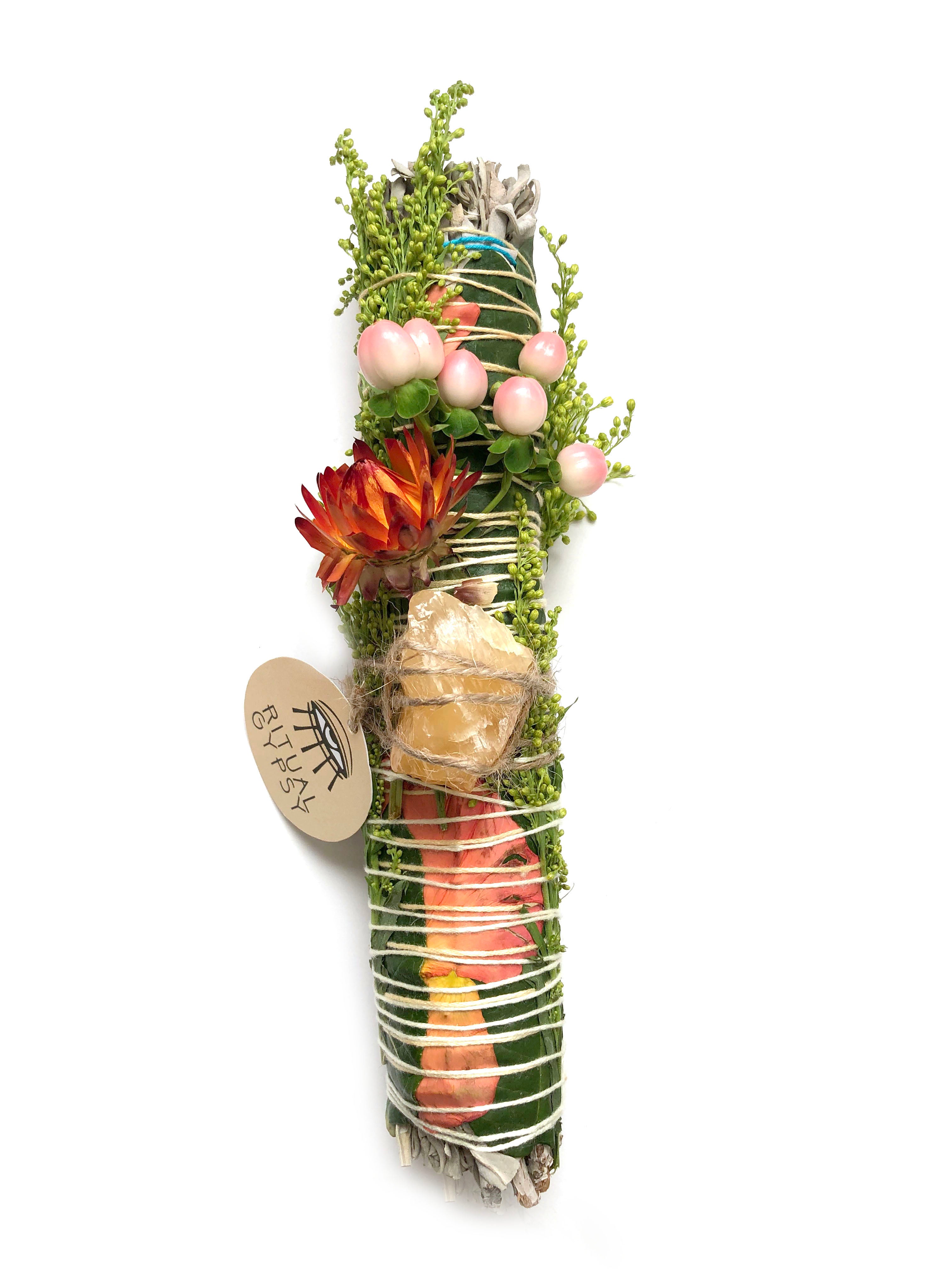 white sage smoke cleansing smudge bundle wrapped in florals with pink strawflower and orange calcite crystal stone and round ritual gypsy product tag attached on white background