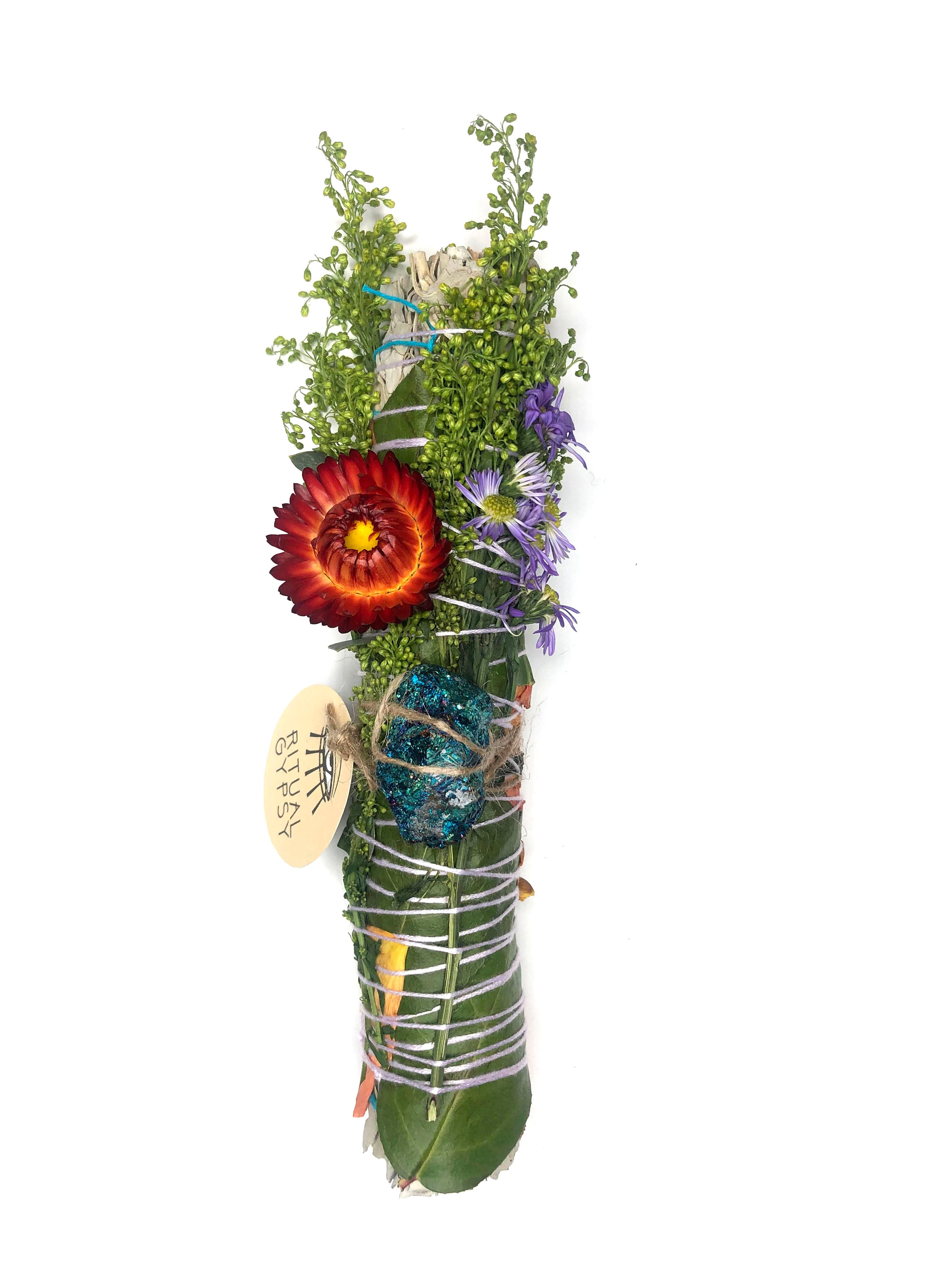 white sage smoke cleansing smudge bundle wrapped in red and yellow rose petals, strawflowers and florals with blue purple peacock ore crystal and round ritual gypsy product tag on white background
