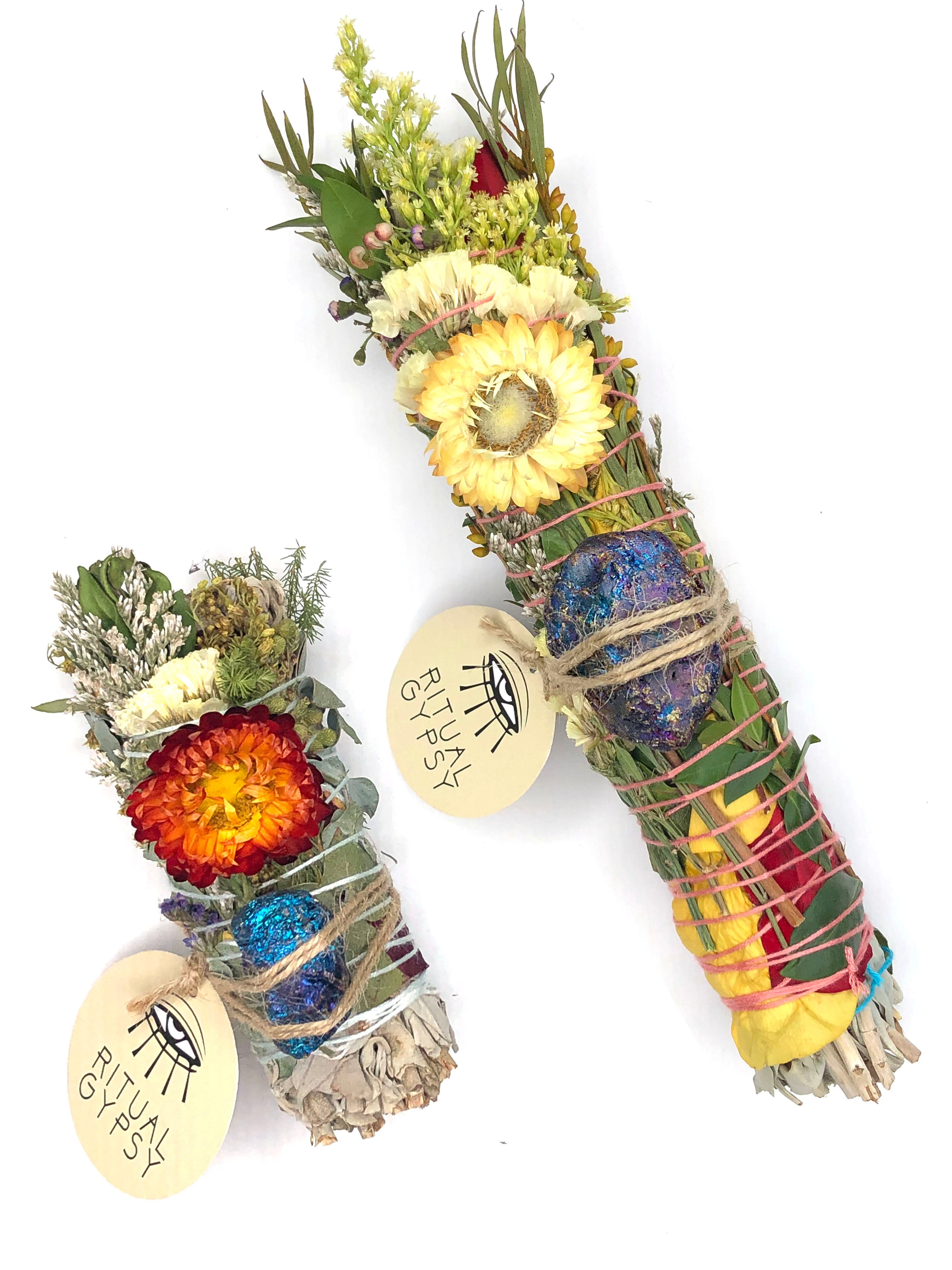 white sage smoke cleansing smudge bundle wrapped in red and yellow rose petals, strawflowers and florals with blue purple peacock ore crystal and round ritual gypsy product tag on white background