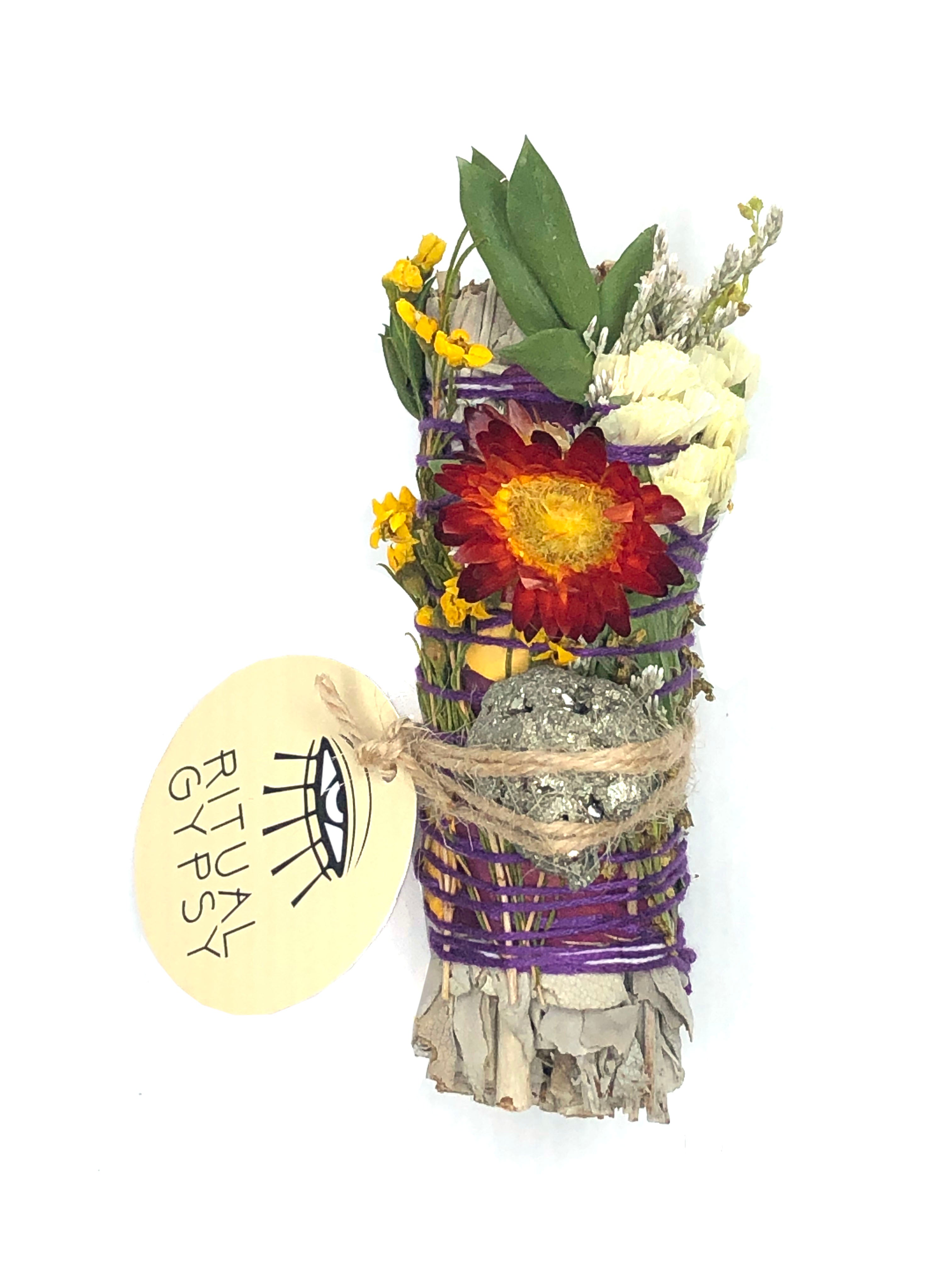 white sage smoke cleansing smudge bundle with white statice, rose petals and red strawflower wrapped in florals with white gold pyrite crystal and round ritual gypsy product tag