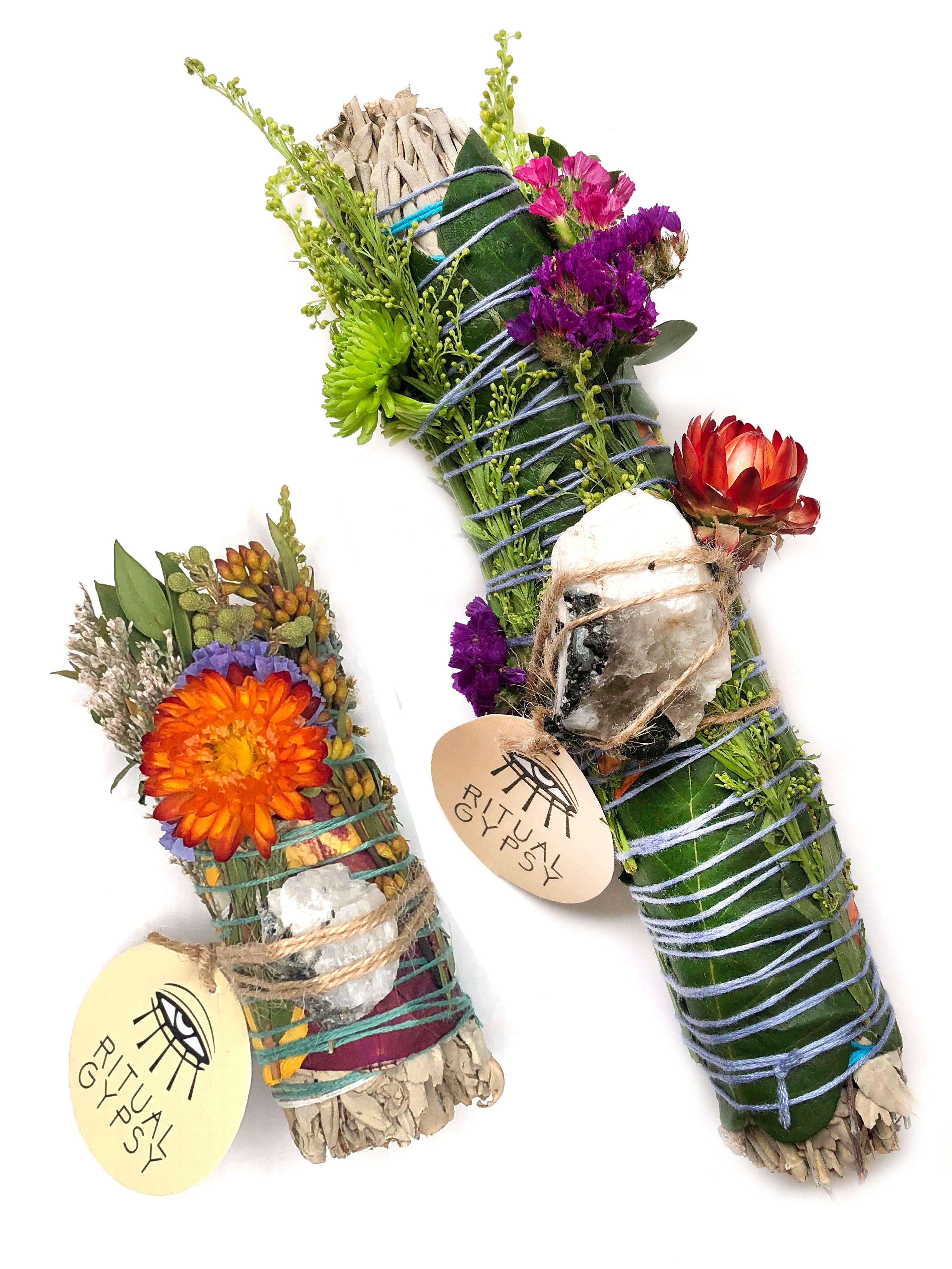 white sage smoke cleansing smudge bundle wrapped in florals with red strawflower and white and black rainbow moonstone crystal and round ritual gypsy product tag attached on white background