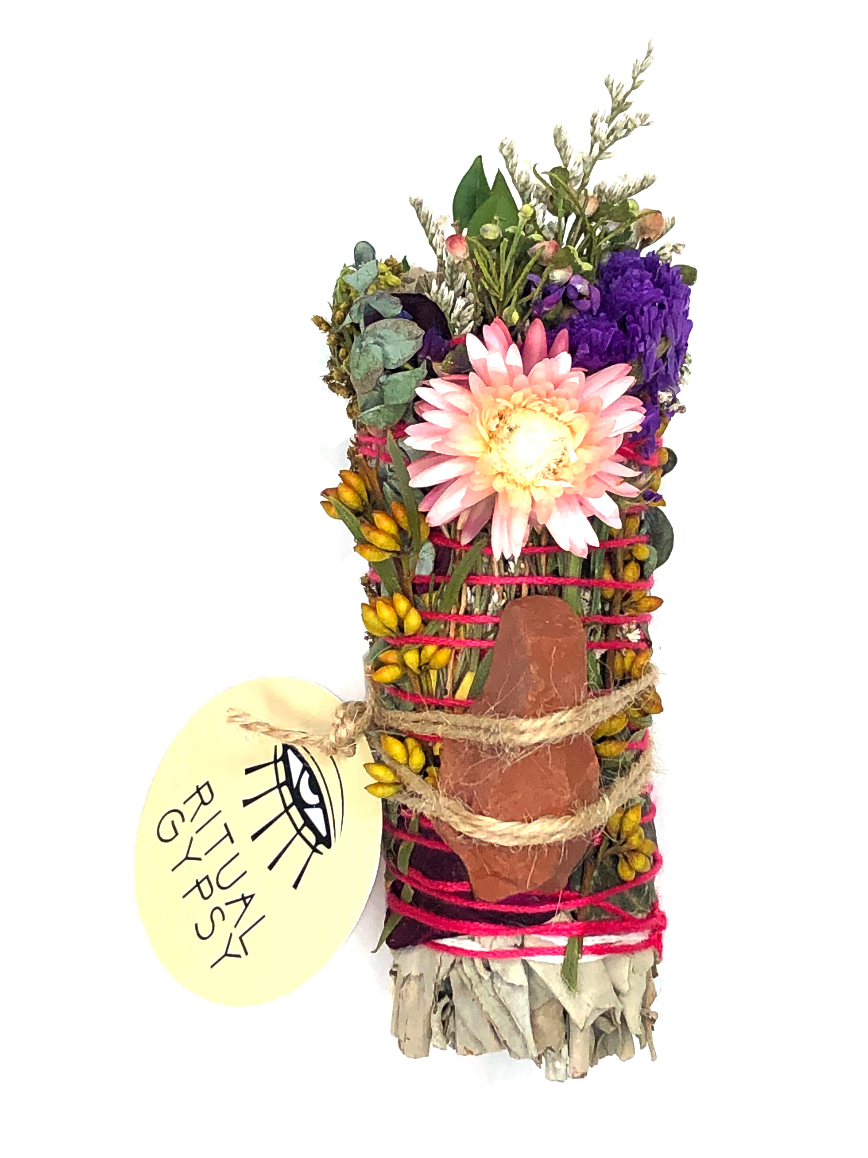 white sage smoke cleansing smudge bundle wrapped in florals with orange pink strawflower and red jasper crystal stone and round ritual gypsy product tag attached on white background