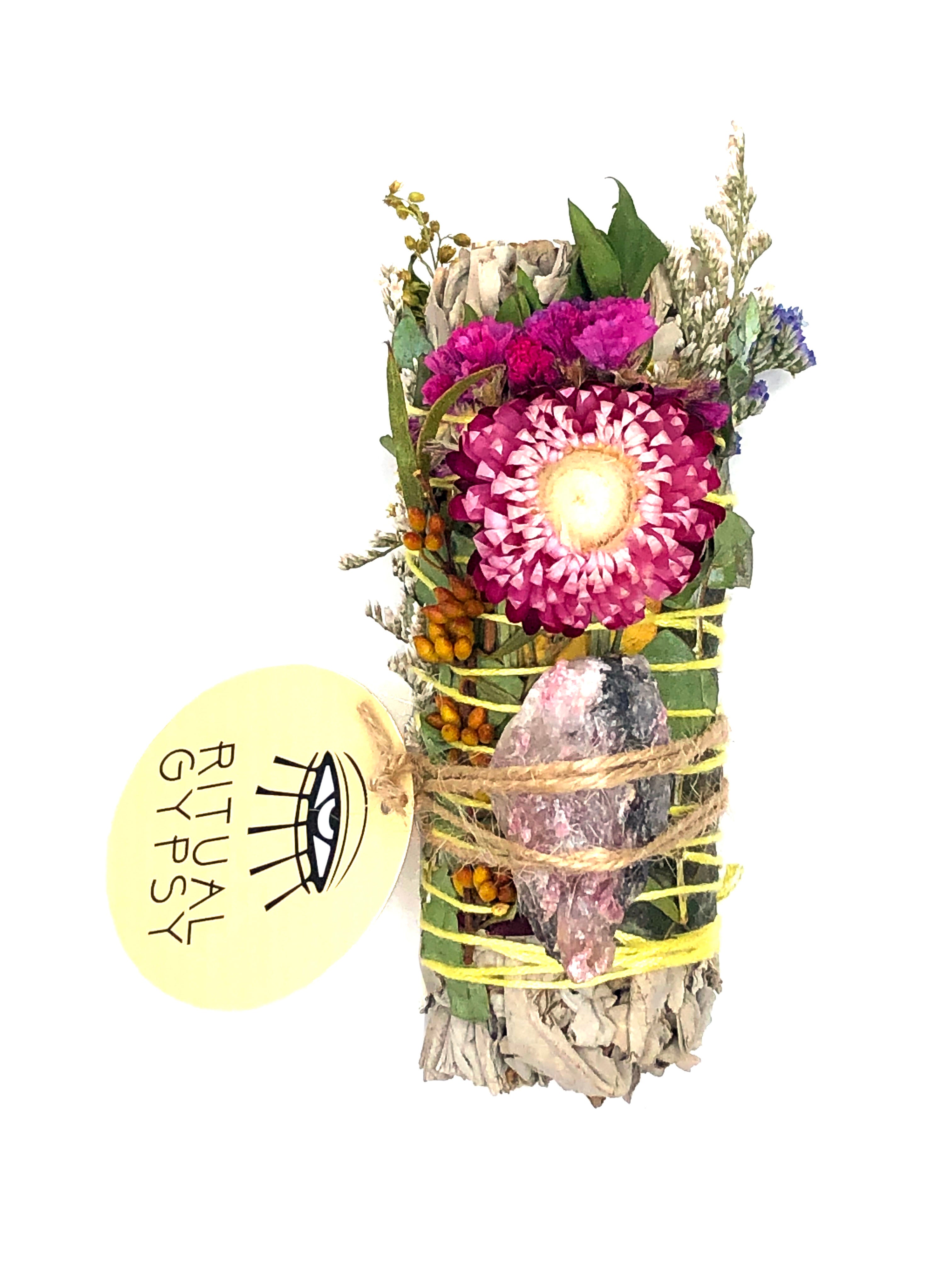 white sage smoke cleansing smudge bundle wrapped in florals with pink strawflower and pink rhodonite crystal and round ritual gypsy product tag on white background