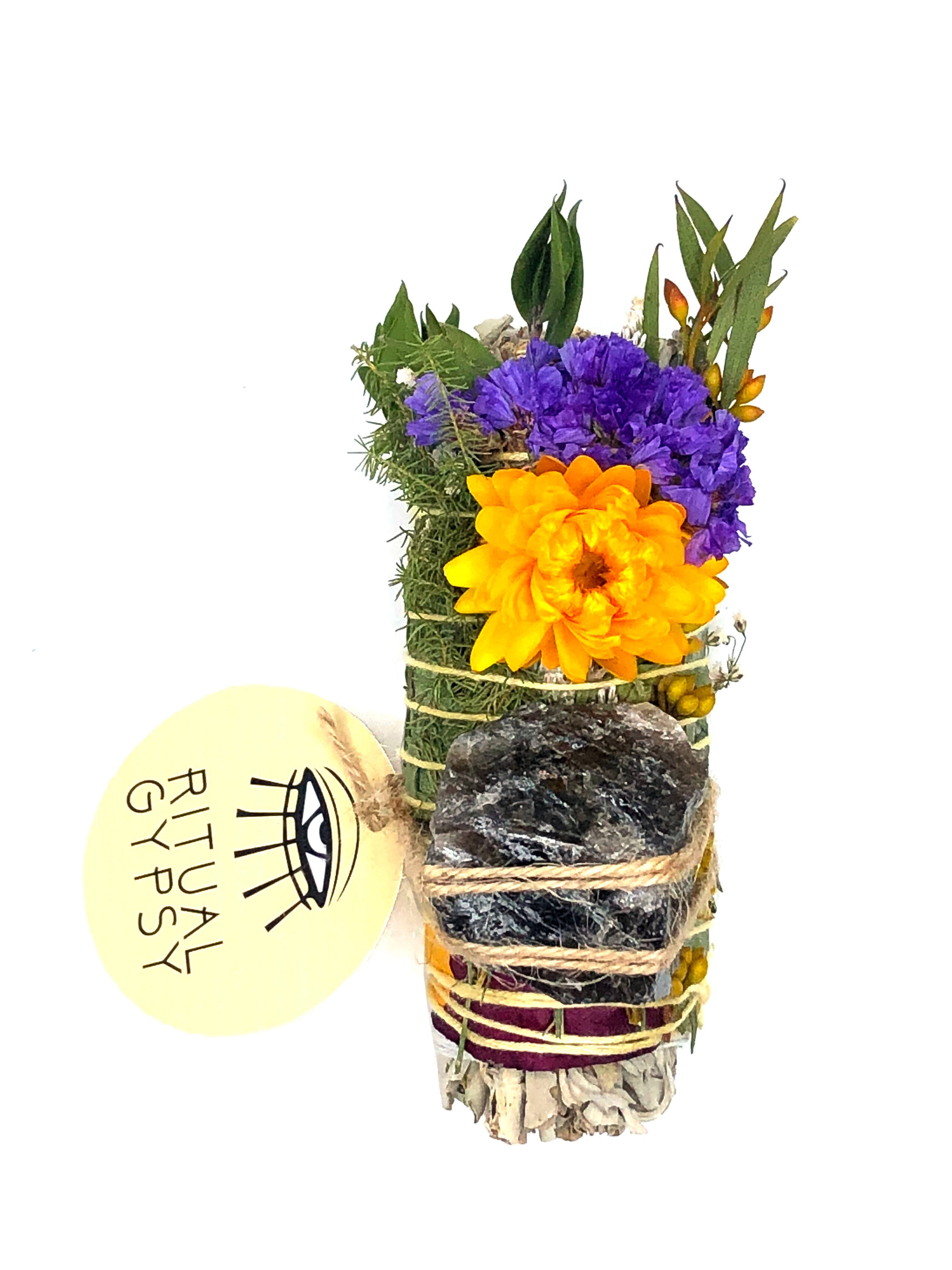 white sage smoke cleansing smudge bundle wrapped in purple florals with orange strawflower and gray black shiny smokey quartz crystal stone and round ritual gypsy product tag attached on white background