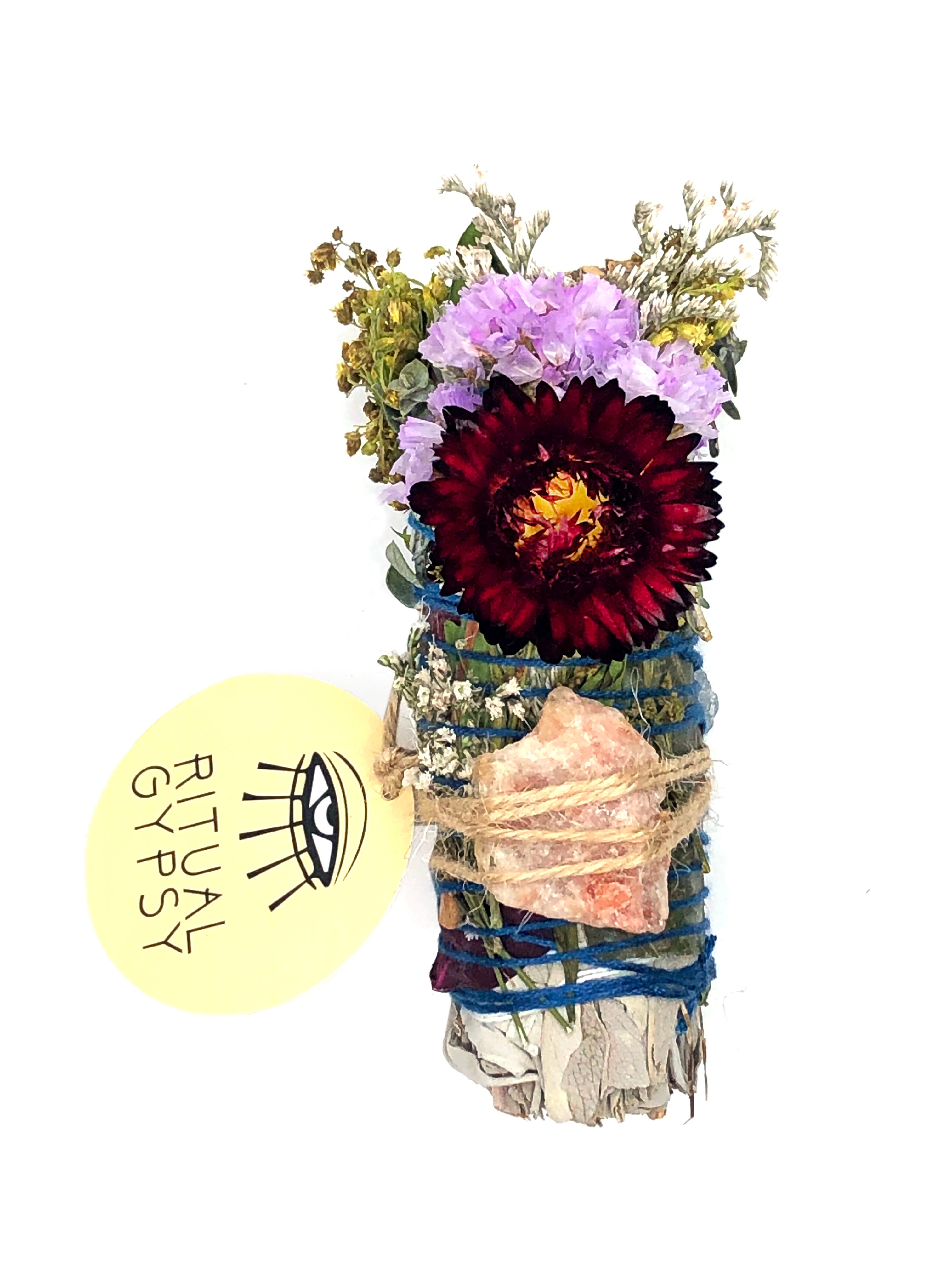 white sage smoke cleansing smudge bundle wrapped in florals with dark red strawflower and florals with orange pink sunstone crystal and round ritual gypsy product tag on white background