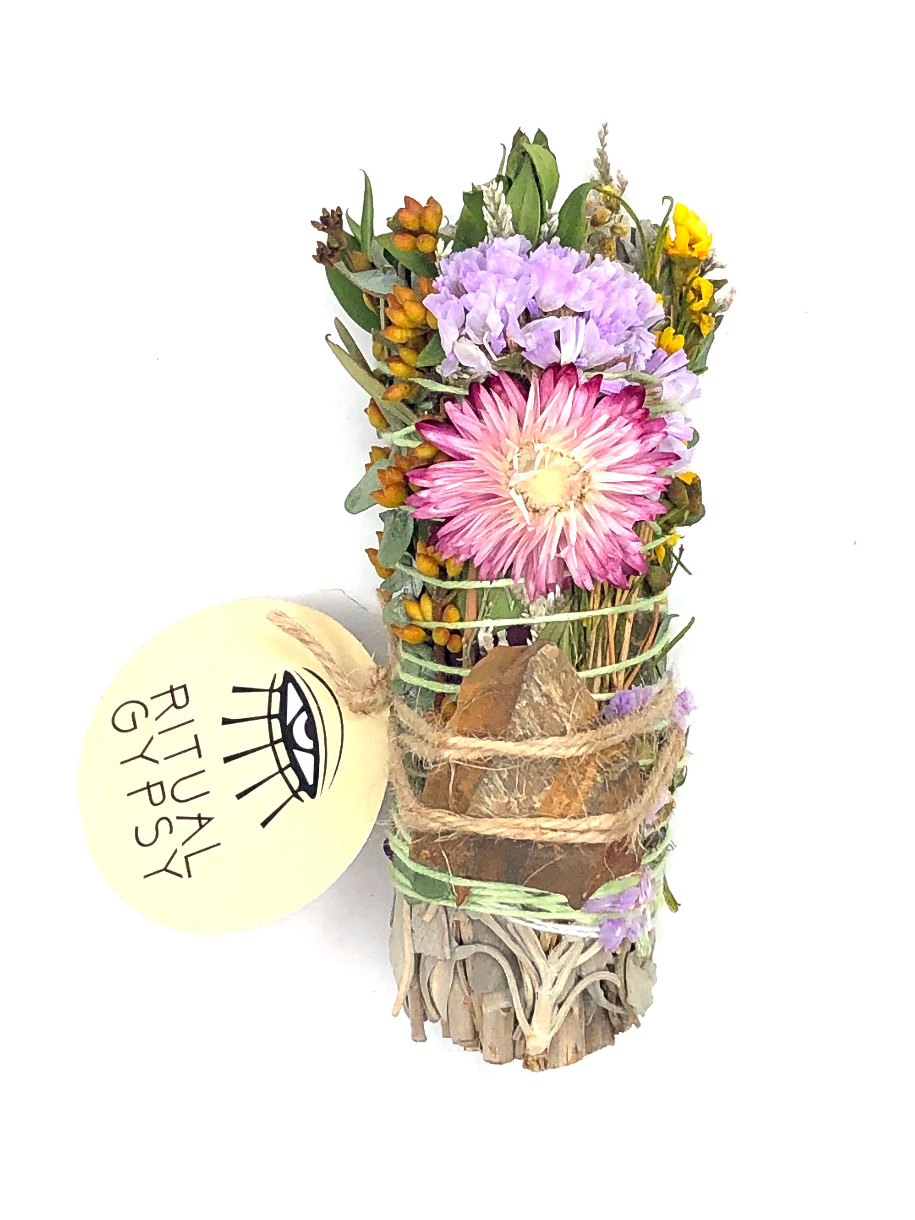 white sage smoke cleansing smudge bundle wrapped in florals with orange pink strawflower and orange brown tan tiger's eye crystal stone and round ritual gypsy product tag attached on white background