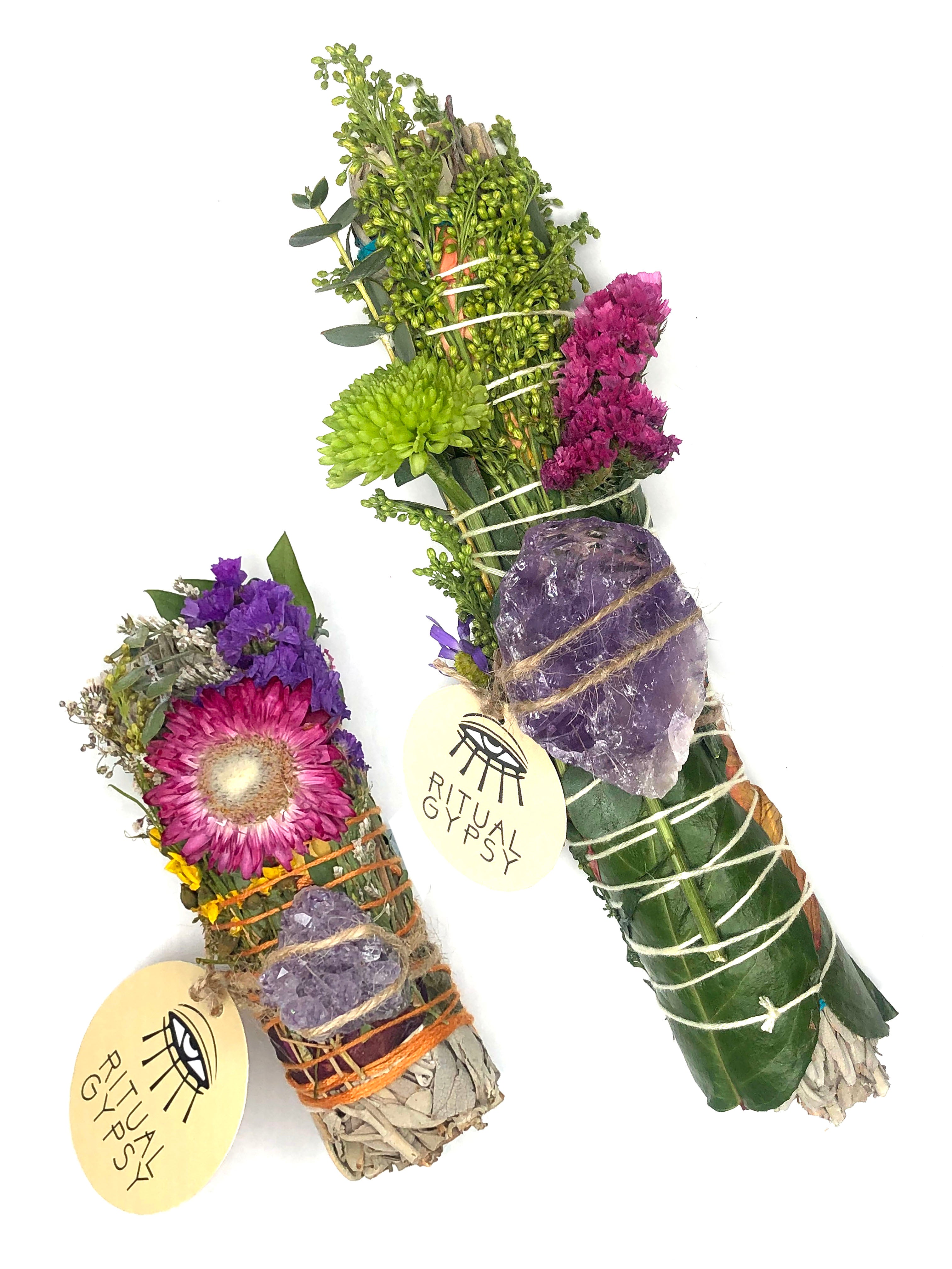 white sage smoke cleansing smudge bundles with pink and purple  statice and pink strawflower wrapped in florals with amethyst crystal and round product tag saying ritual gypsy attached